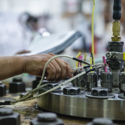 A hand working on a machine with wires and large bolts and nuts.